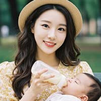 공원 벤치에서 아기에게 젖병을 주며 웃고 있는 예쁜 엄마